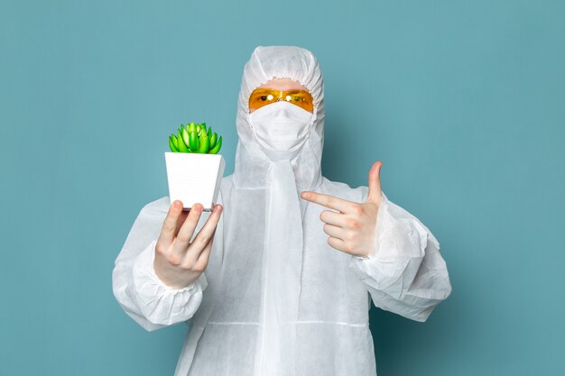 A front view young male in white special suit holding green plant on the blue wall man suit danger special equipment color