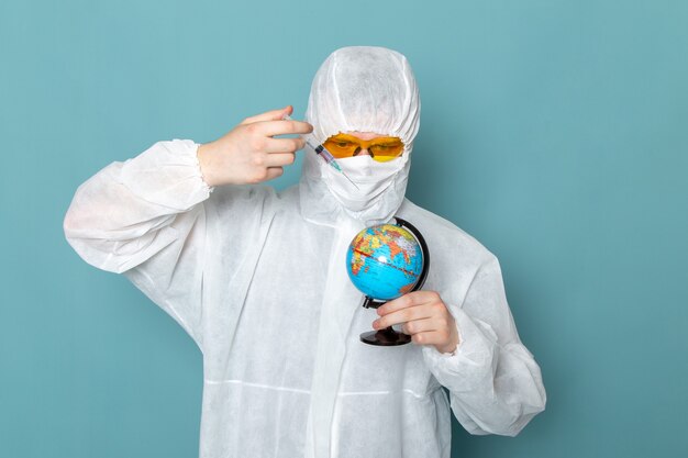 A front view young male in white special suit and holding and injecting little globe on the blue wall man suit danger special equipment color