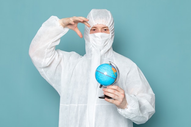 A front view young male in white special suit and holding little globe on the blue wall man suit danger special equipment color