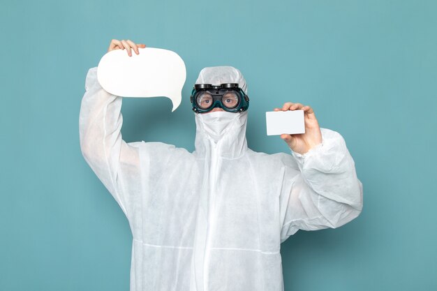 白の特別なスーツと白いカードを保持している正面図の若い男性と青い壁の男のスーツ危険特別装備色