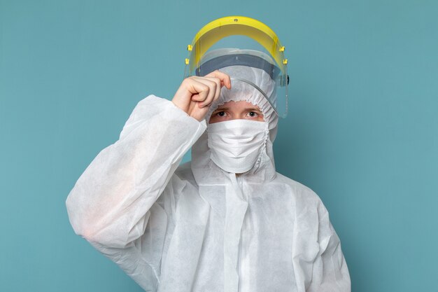 A front view young male in white special suit taking off special head mask on the blue wall man suit danger special equipment color