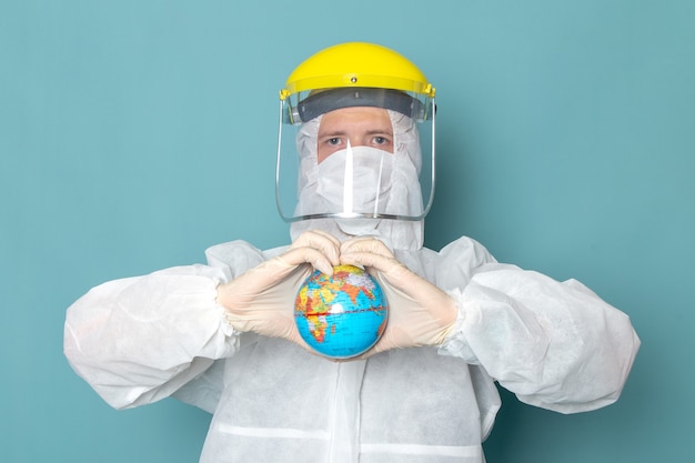 A front view young male in white special suit and yellow special helmet holding globe on the blue wall man suit danger special equipment color