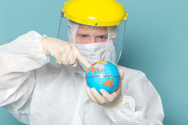 A front view young male in white special suit and yellow special helmet holding globe on the blue wall man suit danger special equipment color