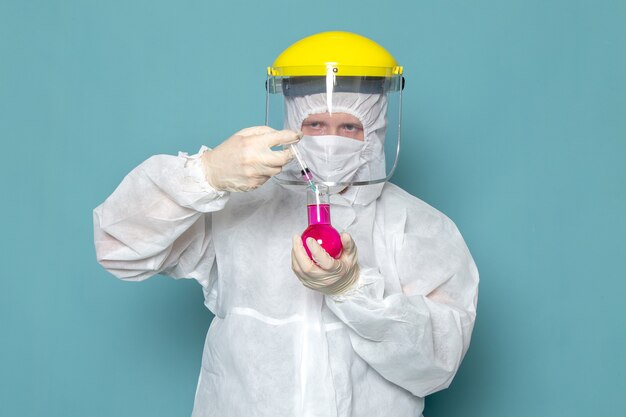 A front view young male in white special suit and yellow special helmet holding solution on the blue wall man suit danger special equipment color