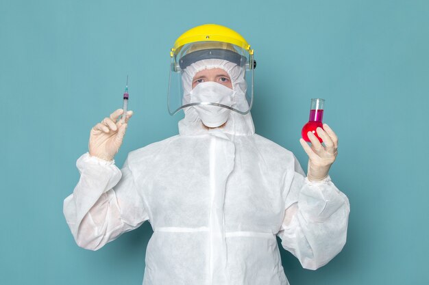 A front view young male in white special suit and yellow special helmet holding solution on the blue wall man suit danger special equipment color