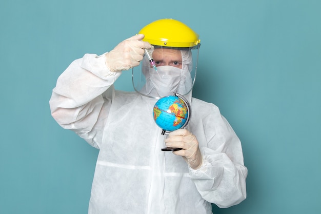 A front view young male in white special suit and yellow special helmet injecting little globe on the blue wall man suit danger special equipment color