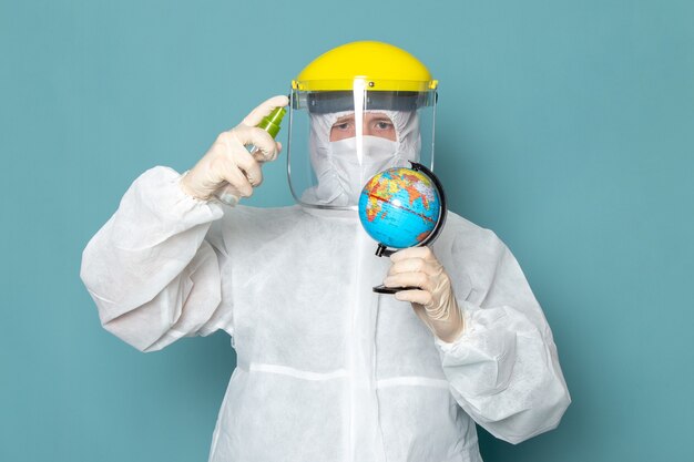 A front view young male in white special suit and yellow special helmet using spray on the blue wall man suit danger special equipment color