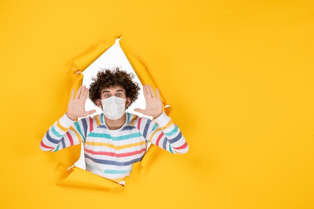 Free photo front view young male in white sterile mask on yellow ripped color covid- health human photo pandemic virus