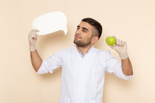 Front view young male in white suit wearing gloves holding white sign and apple on beige