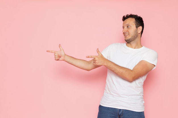 Foto gratuita un giovane maschio di vista frontale in maglietta bianca e blue jeans che posa e che sorride sulla posa rosa di emozione di colore dell'uomo dello scrittorio