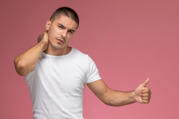 Front view young male in white t-shirt having a neckache on the pink background  