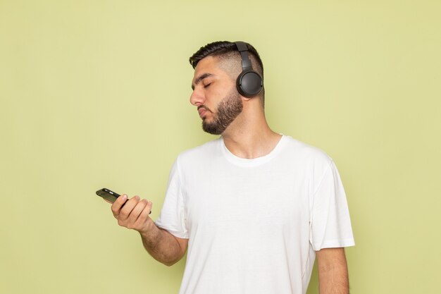 A front view young male in white t-shirt holding phone and listening to music