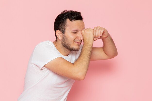 A front view young male in white t-shirt looking through his fingers