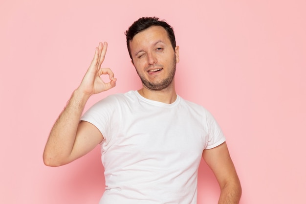 申し分のない兆しを見せている白いtシャツのポーズで正面の若い男性