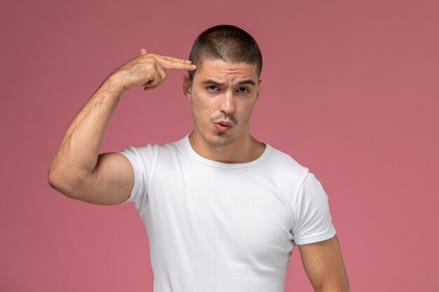 Front view young male in white t-shirt posing touching his temple on pink background 