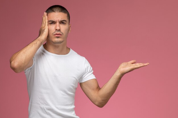 Front view young male in white t-shirt posing with depressed expression on pink background  