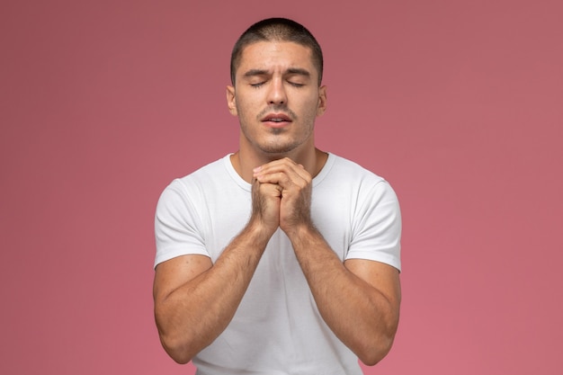 Front view young male in white t-shirt in prayer posing on pink background 