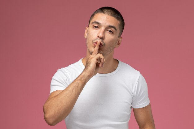 Front view young male in white t-shirt showing silence sign on pink background 