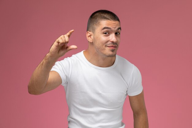 Вид спереди молодой мужчина в белой футболке показывает размер пальцами на розовом фоне
