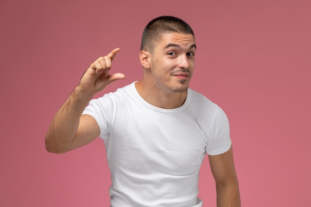 Front view young male in white t-shirt showing size with his fingers on pink background 