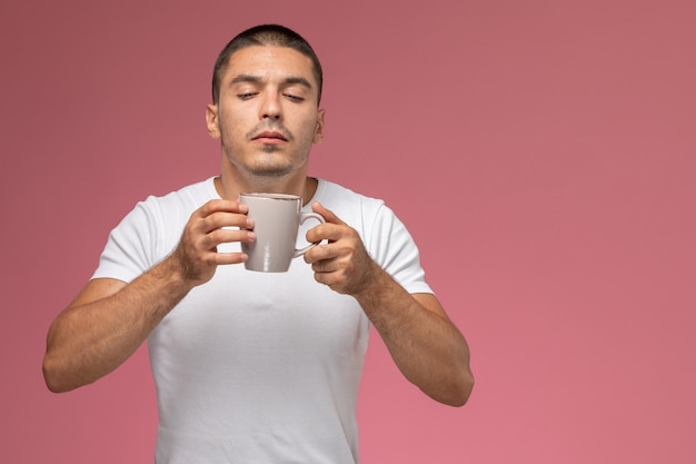 ピンクの背景にコーヒーの香りの白いtシャツの正面の若い男性