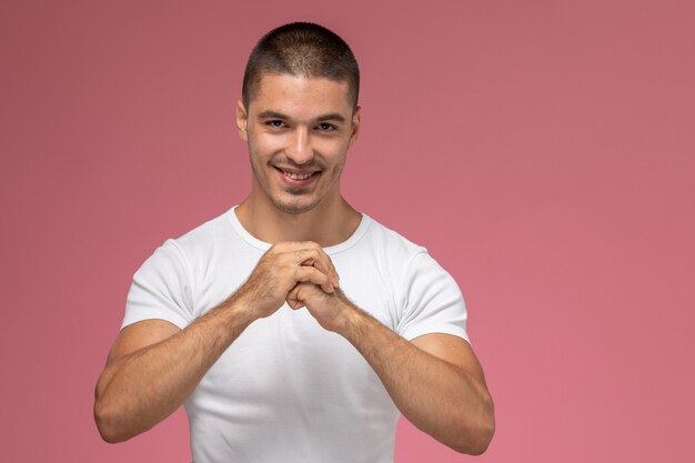 Front view young male in white t-shirt smiling and squeezing his fists on pink background  