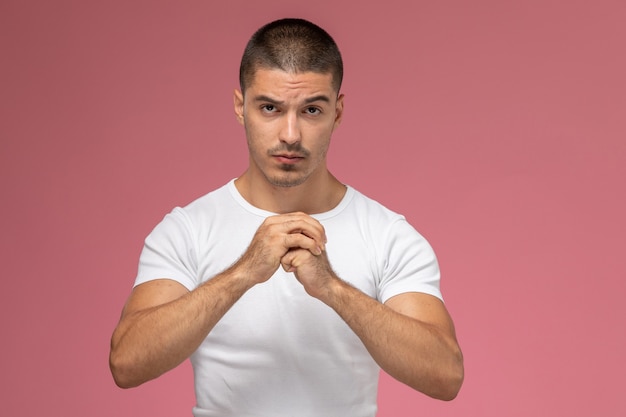 Front view young male in white t-shirt squeezing his fists on pink background  