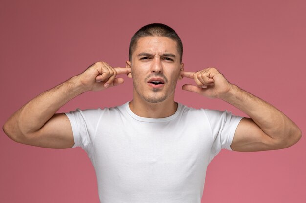 Front view young male in white t-shirt stucking his ears on pink background  