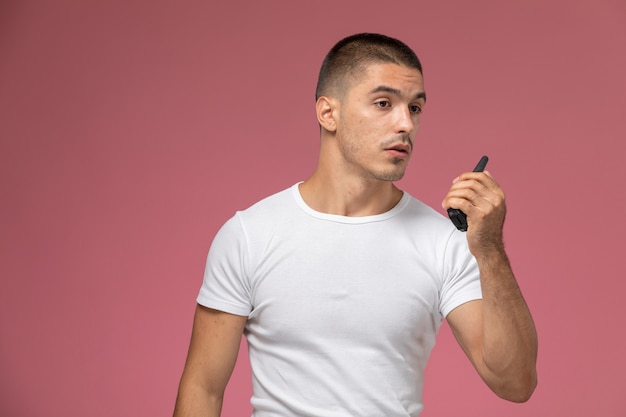 Front view young male in white t-shirt using walkie-talkie on the pink background  