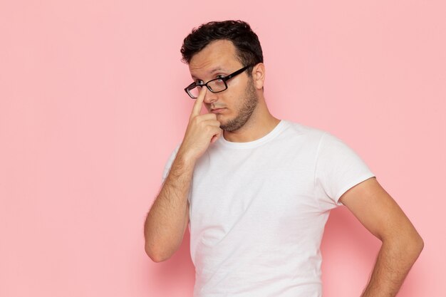 A front view young male in white t-shirt wearing optical sunglasses on the pink desk man color emotion pose