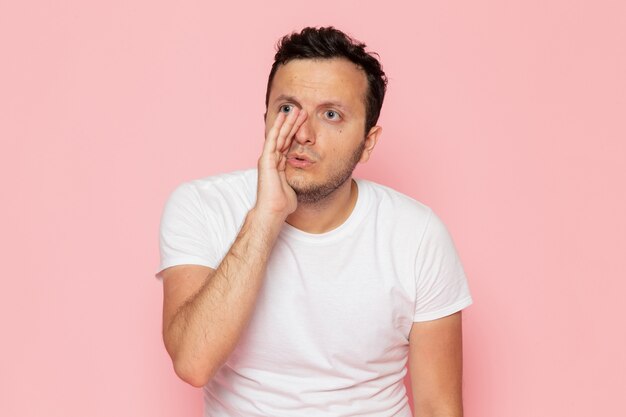 A front view young male in white t-shirt whispering on the pink desk man color emotion pose