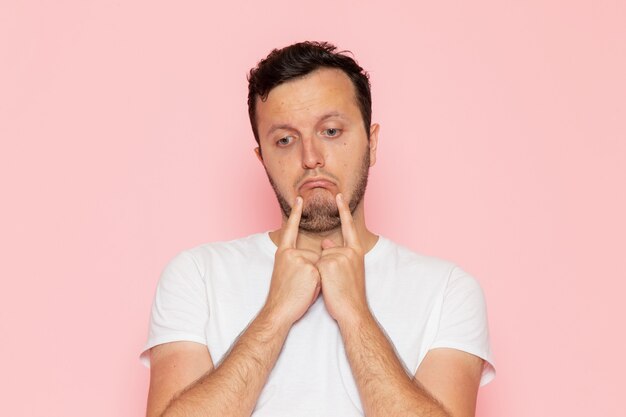 A front view young male in white t-shirt with saddened expression on the pink desk man color emotion pose