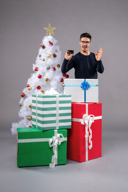 Front view young male with bank card and presents on grey