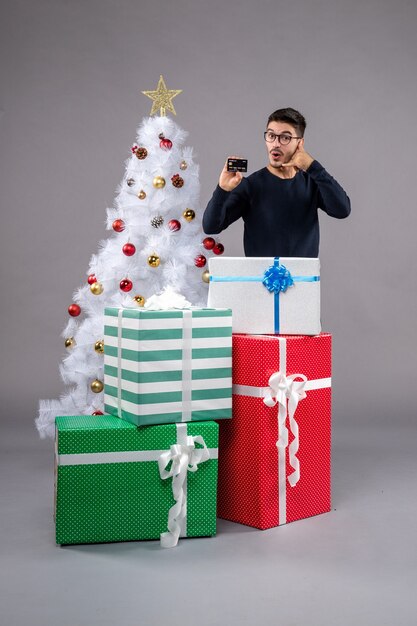 Вид спереди молодой мужчина с банковской картой и подарками на сером