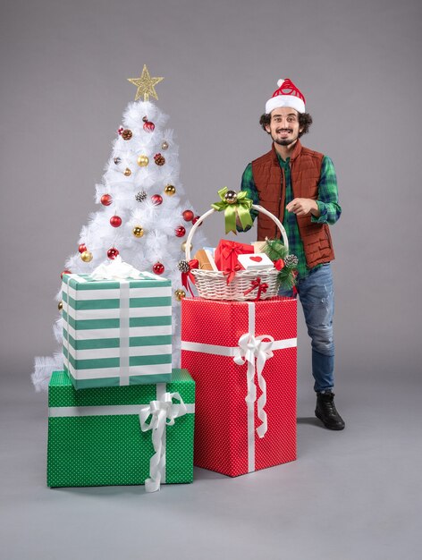 Вид спереди молодой мужчина с корзиной вокруг подарков на сером столе новогодний рождественский человек