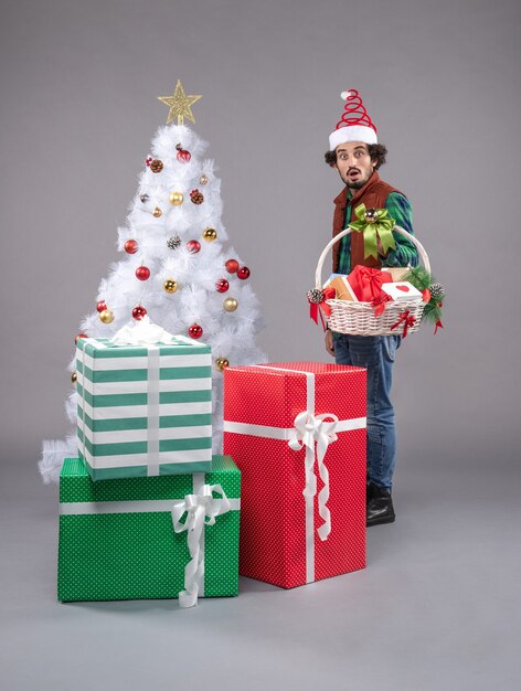 Вид спереди молодой мужчина с корзиной вокруг подарков на сером