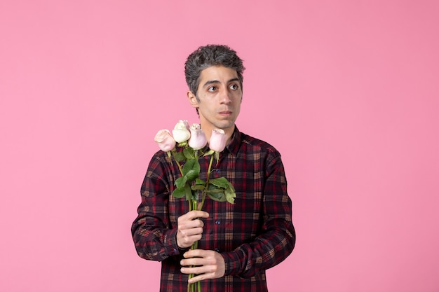 Vista frontale giovane maschio con bellissime rose rosa sul muro rosa Foto Gratuite
