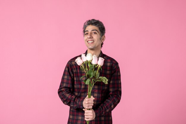 ピンクの壁に美しいピンクのバラと正面図若い男性