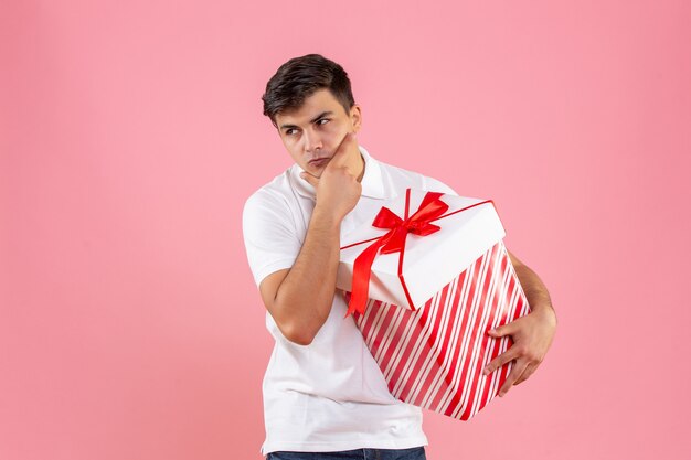 Вид спереди молодой самец с большим рождественским подарком, думающий на розовом фоне