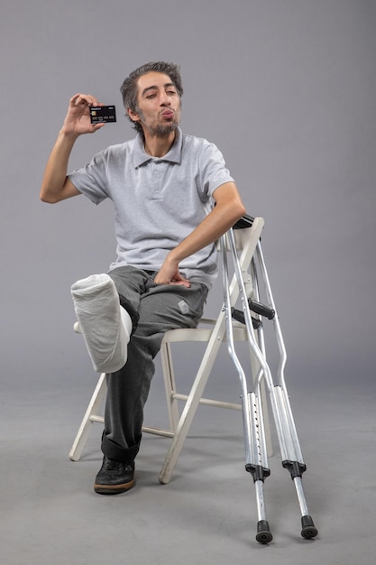 Free photo front view young male with broken foot and bandage holding black bank card on the grey wall human twist male accident foot pain