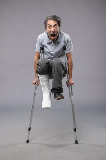 Free photo front view young male with broken foot screaming from pain on grey wall legs twist accident pain broken foot