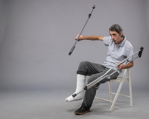 Front view young male with broken foot using crutches for walking on a grey floor foot broken pain twist accident leg