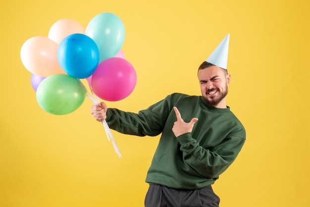Front view young male with colorful balloons on the yellow background