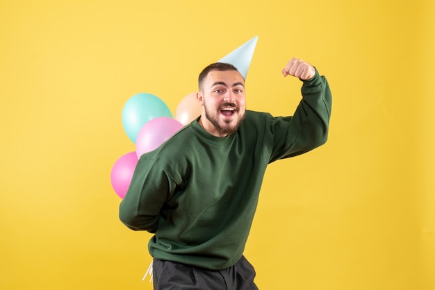 Giovane maschio di vista frontale con palloncini colorati su sfondo giallo