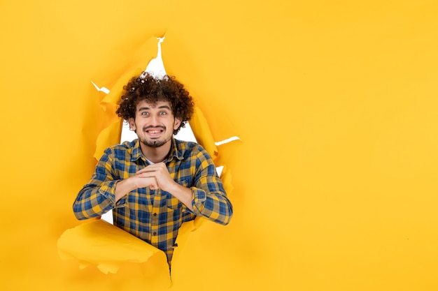 Foto gratuita giovane maschio di vista frontale con capelli ricci che sorride sul fondo strappato giallo