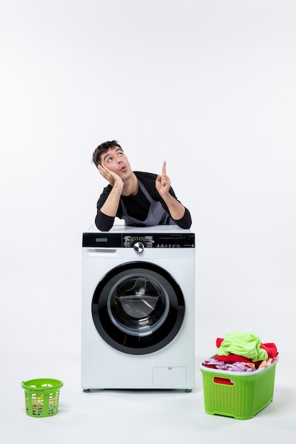 Front view of young male with dirty clothes and washer on a white wall