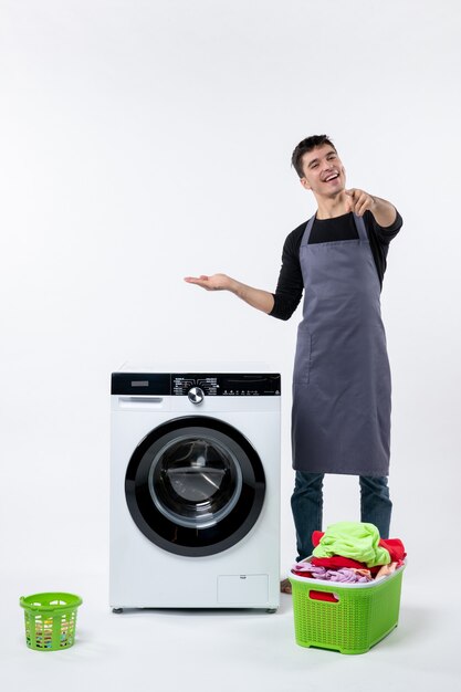 汚れた服と白い壁に洗濯機を持つ若い男性の正面図