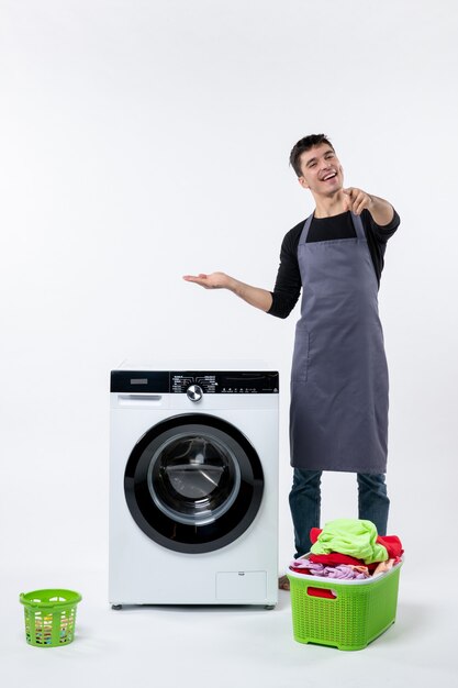 Front view of young male with dirty clothes and washer on the white wall