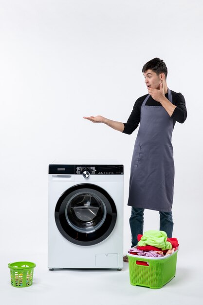 汚れた服と白い壁に洗濯機を持つ若い男性の正面図