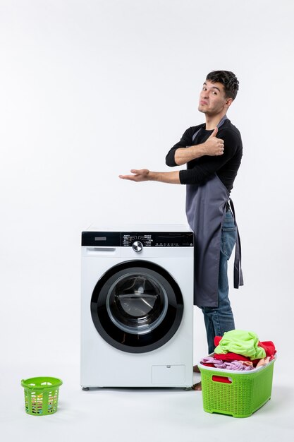 Front view of young male with dirty clothes and washer on white wall